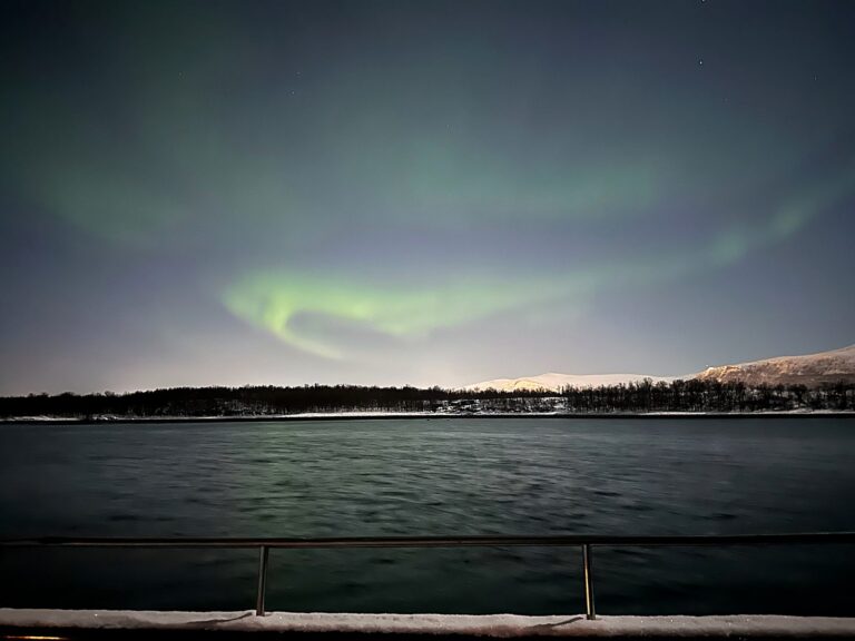 Northern lights glowing over dark Arctic water from a boat near Tromsø, Norway
