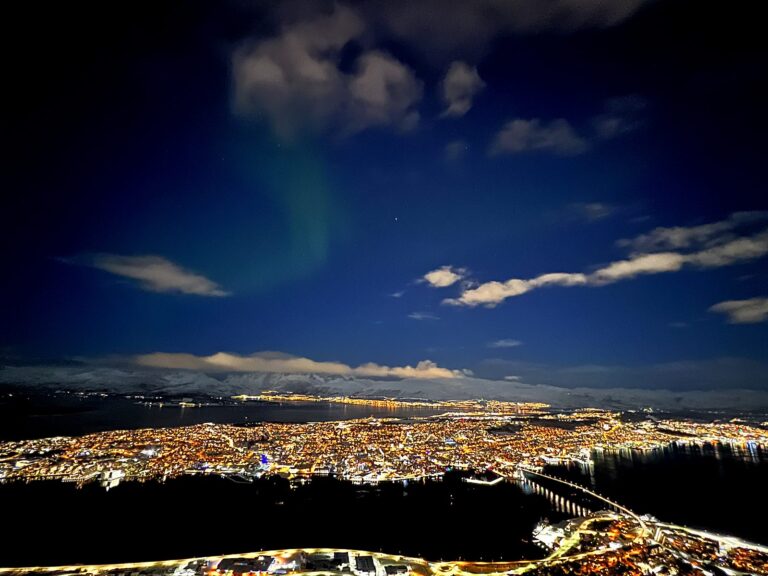 Aurora borealis above the illuminated city and bridge of Tromsø during polar night