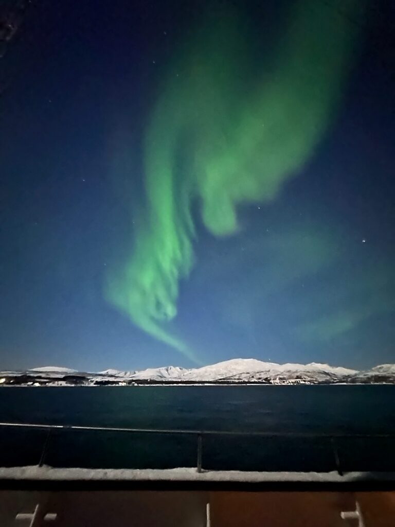 Bright green northern lights ribbons overhead seen from the deck of an aurora cruise near Tromsø