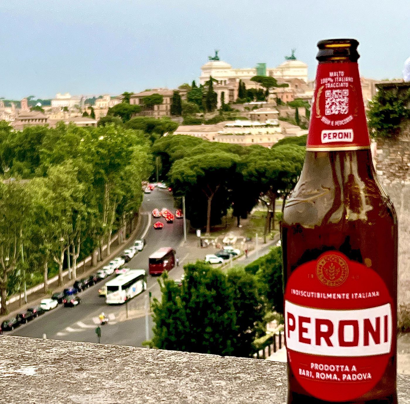 A cold Peroni on a stone wall at a green Rome viewpoint looking toward the Vittoriano