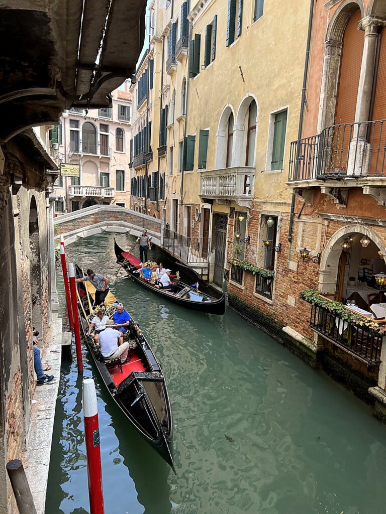 Gondolas full of visitors gliding through a narrow Venice canal in summer